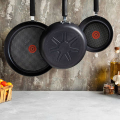 Three nonstick frying pans with red heat indicators hang on a kitchen wall.