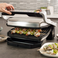 A hand hovers over the T-fal OptiGrill's lid, grilling skewers of shrimp and vegetables