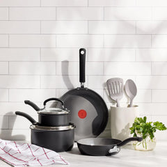 Set of black ceramic cookware and nylon utensils on a kitchen counter with white tile backsplash.
