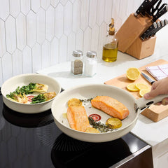 Two beige frying pans with detachable handles on an induction stove cooking colorful meals