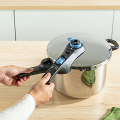 Hands closing a stainless pressure cooker lid with black and blue handles on wood counter