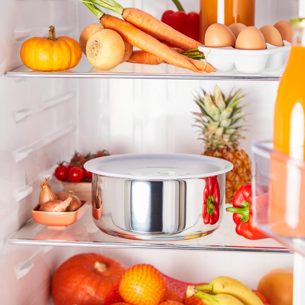 Stainless steel bowl with lid on fridge shelf surrounded by various fruits and vegetables