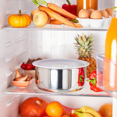 Stainless steel bowl with lid on fridge shelf surrounded by various fruits and vegetables