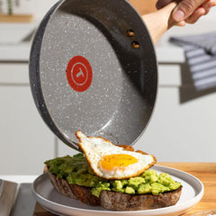 A ceramic frying pan serves a fried egg onto avocado toast.