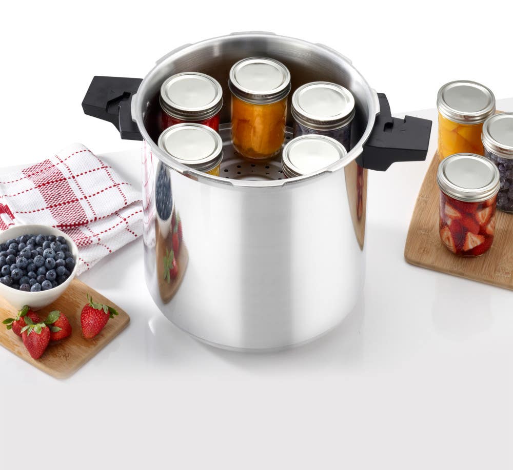 T-fal pressure canner containing jars of preserves, surrounded by bowls of berries and a folded cloth.