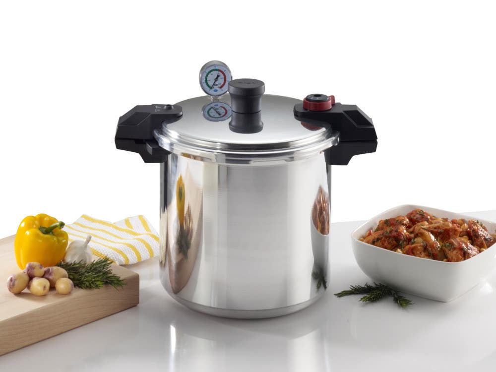 Stainless steel pressure cooker with black handles, pressure gauge on lid, and a pot of stew beside fresh vegetables.