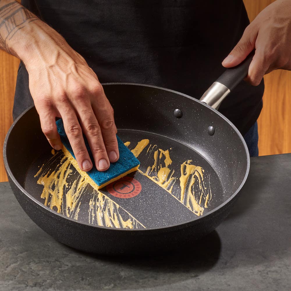 Hand cleaning a Stone Force Frying Pan with a sponge.