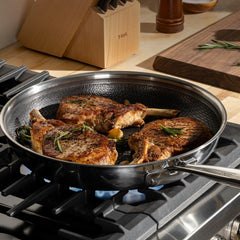 Three seasoned pork chops cooking in a stainless steel frying pan with non-stick interior