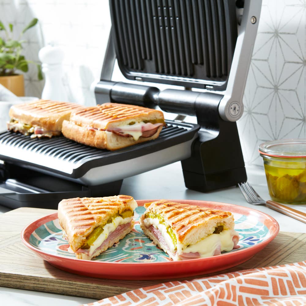 Two ham and cheese paninis grilling on a T-fal OptiGrill. A sliced panini on a plate in the foreground.