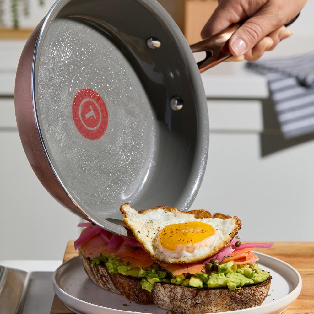 Fried egg being transferred from grey pan with a red Thermospot onto avocado toast. Green label reads "Made without PFOA & PTFE