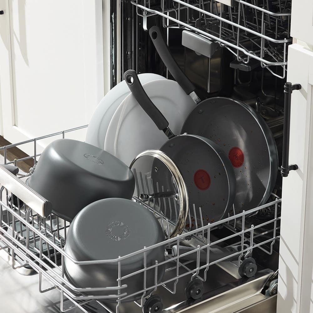 Nonstick cookware and lids loaded in the bottom rack of a dishwasher.