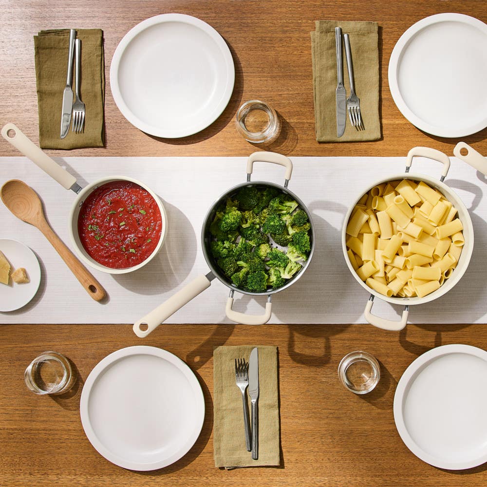 Overhead view of beige nonstick cookware showing pasta, broccoli and tomato sauce on a table set for dinner