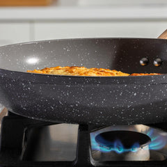 Close-up of a grey speckled ceramic frying pan on a gas stove with food cooking inside