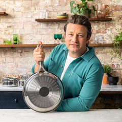 Chef in teal shirt showing stainless frypan with induction base in bright rustic kitchen