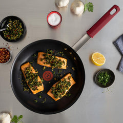 Three salmon fillets with green herb sauce in a t-fal nonstick frypan beside garlic, lemon and herbs