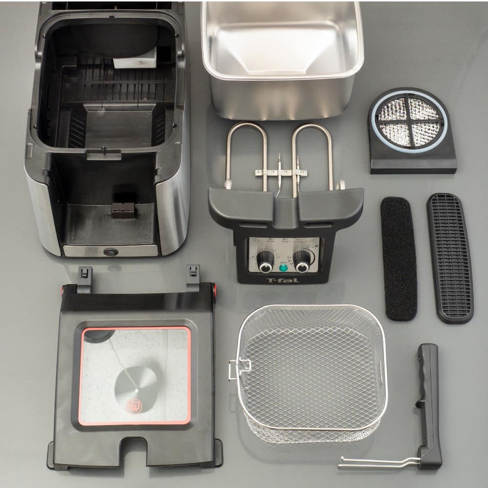Various components of the T-Fal advanced deep fryer: main unit, stainless steel container, heating element, basket, safety lid, and filters, neatly arranged on a surface.