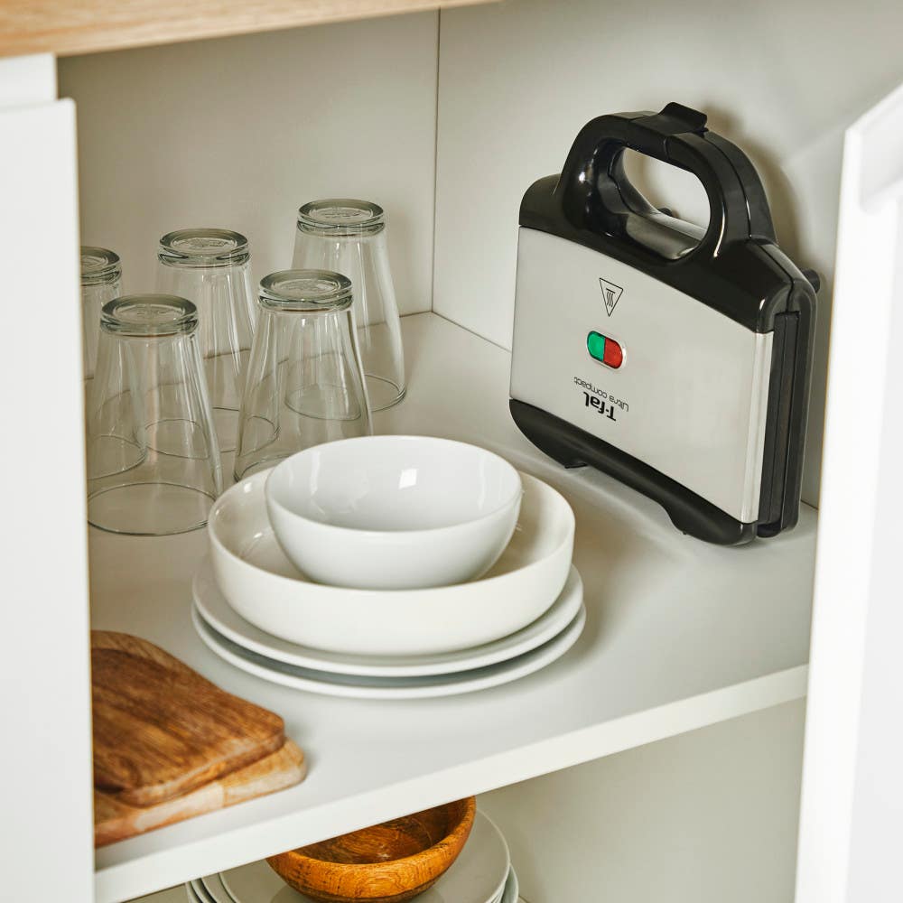 Sandwich maker stored vertically in kitchen cabinet with plates and glasses.
