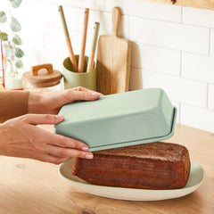 Hands lifting a mint green loaf pan from freshly baked banana bread on a kitchen counter.