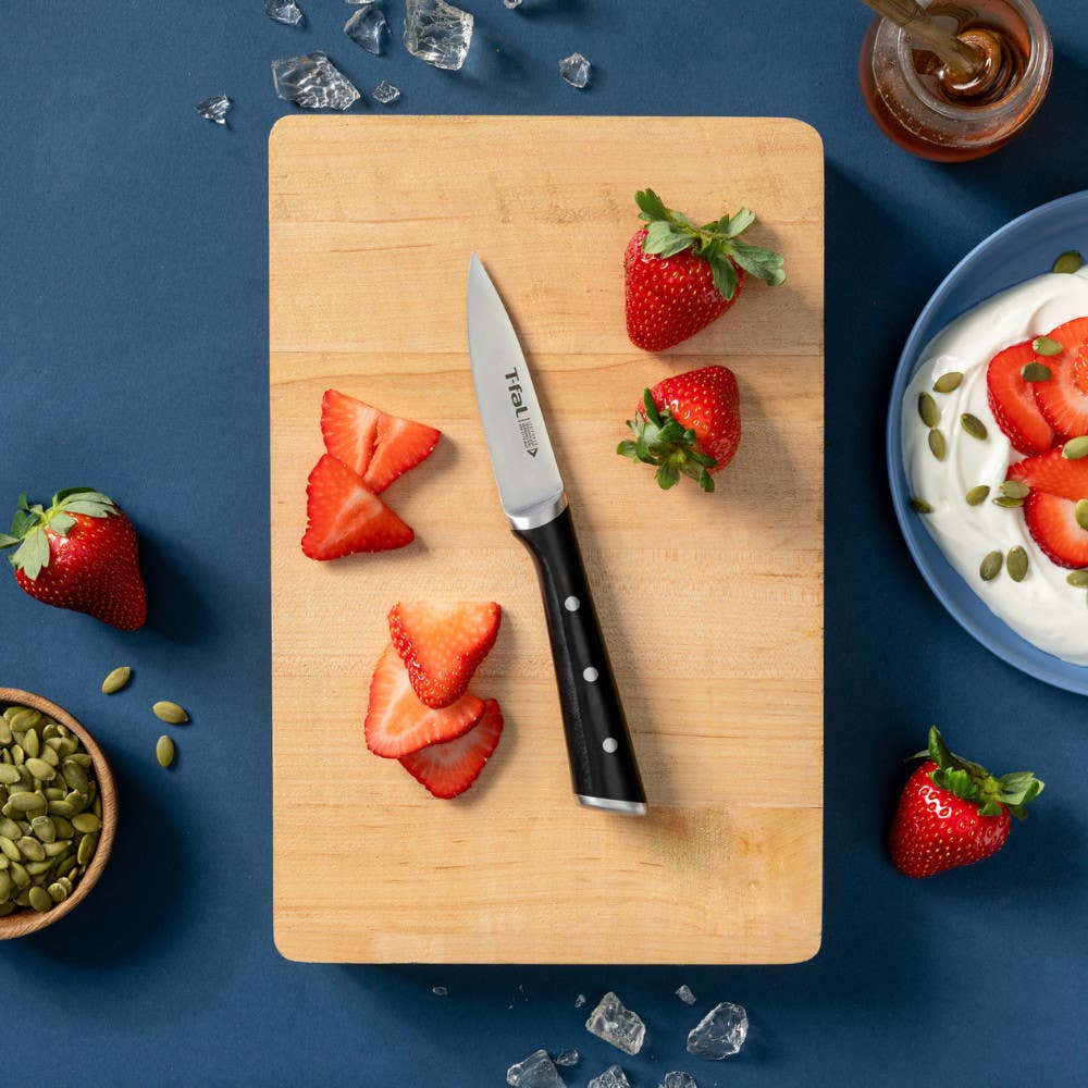 Cutting board with strawberries and paring knife, surrounded by food on blue background.