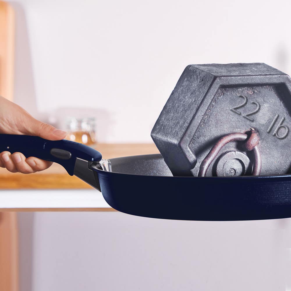 A blue frying pan holding a grey 22 lb weight, with a hand grasping the handle
