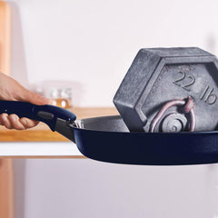 A blue frying pan holding a grey 22 lb weight, with a hand grasping the handle