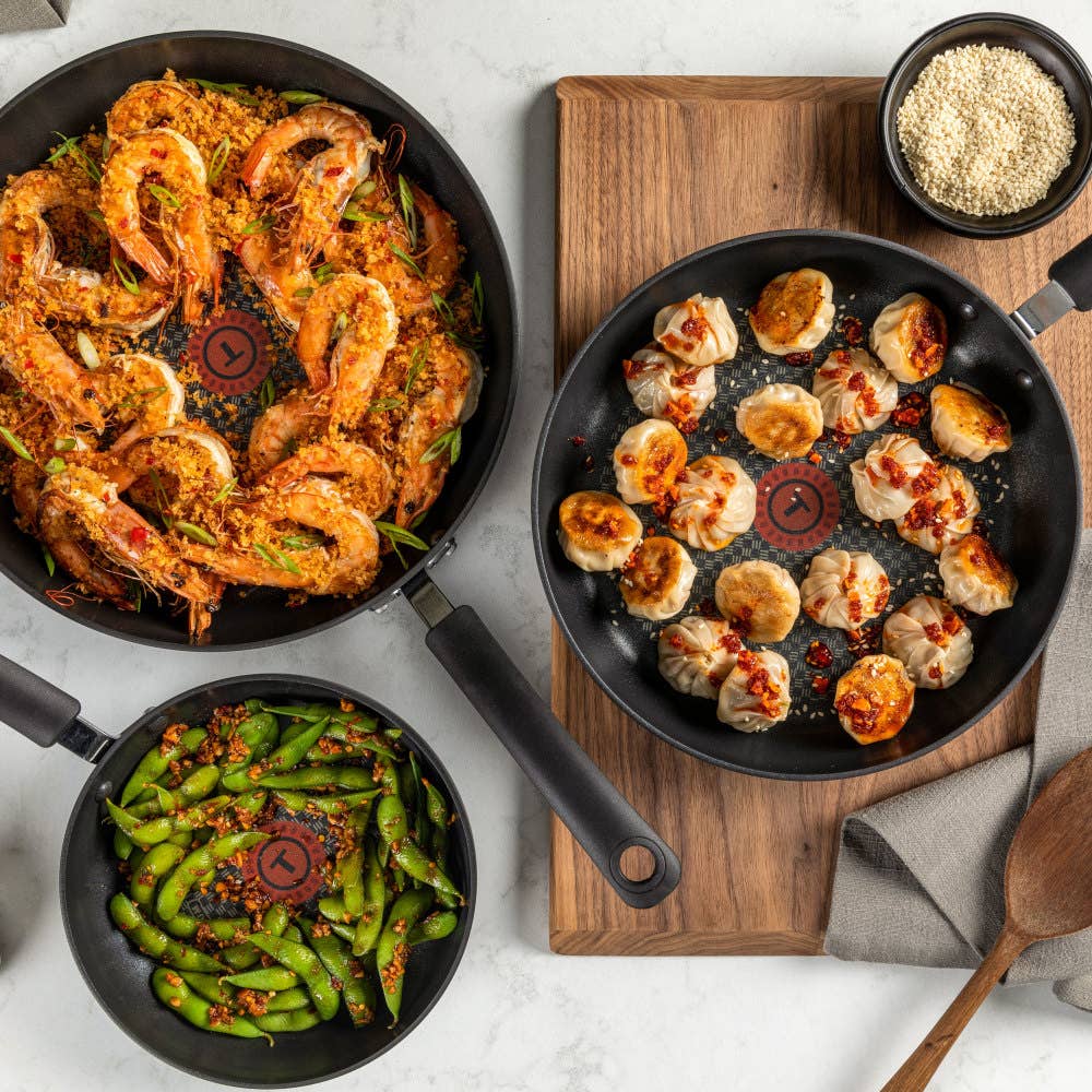 Three Ultimate Hard Anodized pans with different cooked dishes: shrimp, dumplings, and vegetables.