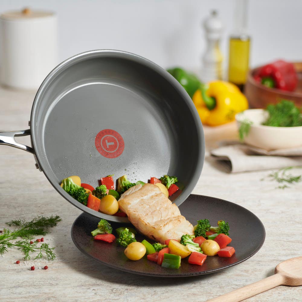 Fish and vegetables being served from a pan onto a black plate