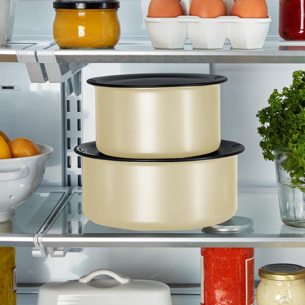 Stacked beige pots with black lids in a refrigerator, surrounded by other food items