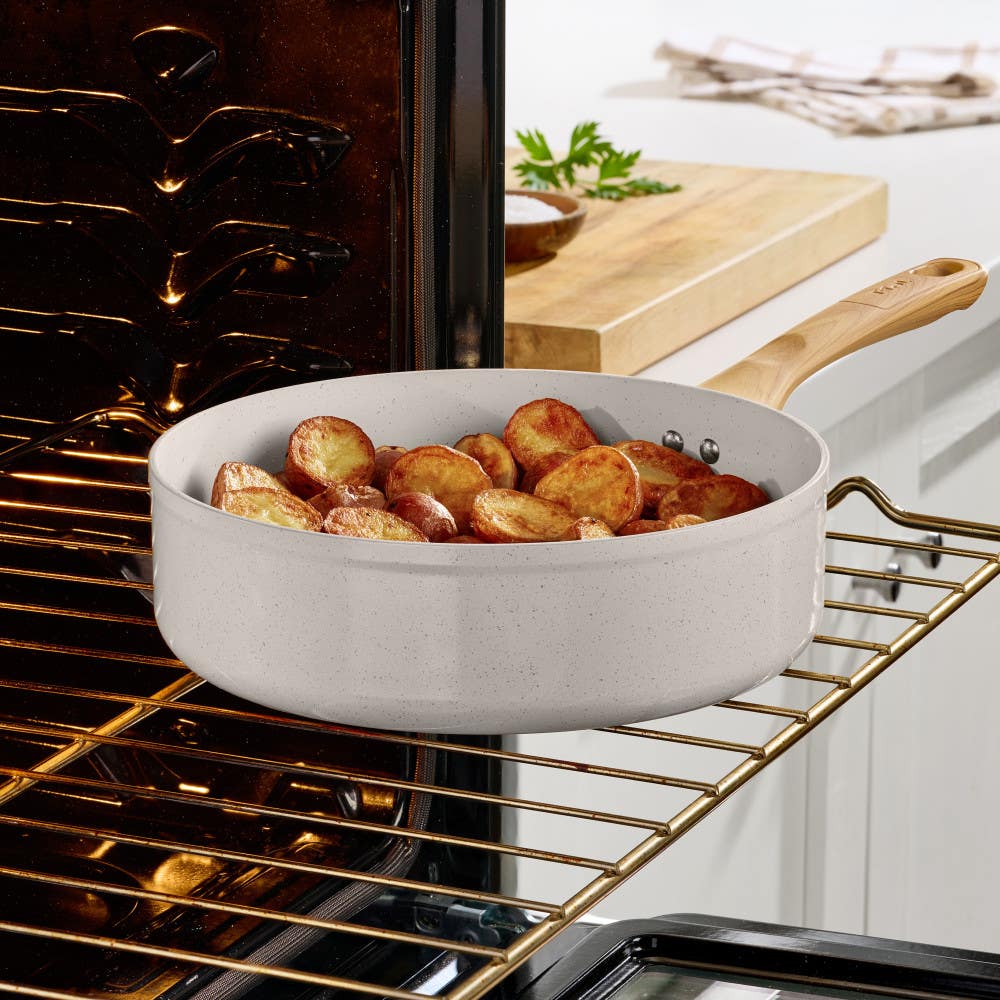 Beige ceramic jumbo cooker with roasted potatoes, placed in an oven on the oven rack