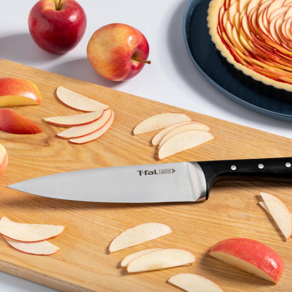 Sliced apples and T-fal chef's knife on cutting board, with apple tart in the background.