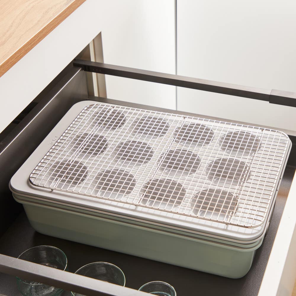 Stacked baking trays with cooling rack, inside an open kitchen drawer.