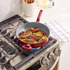 Red deep sauté pan with seasoned chicken, lemon slices and radishes on gas stove