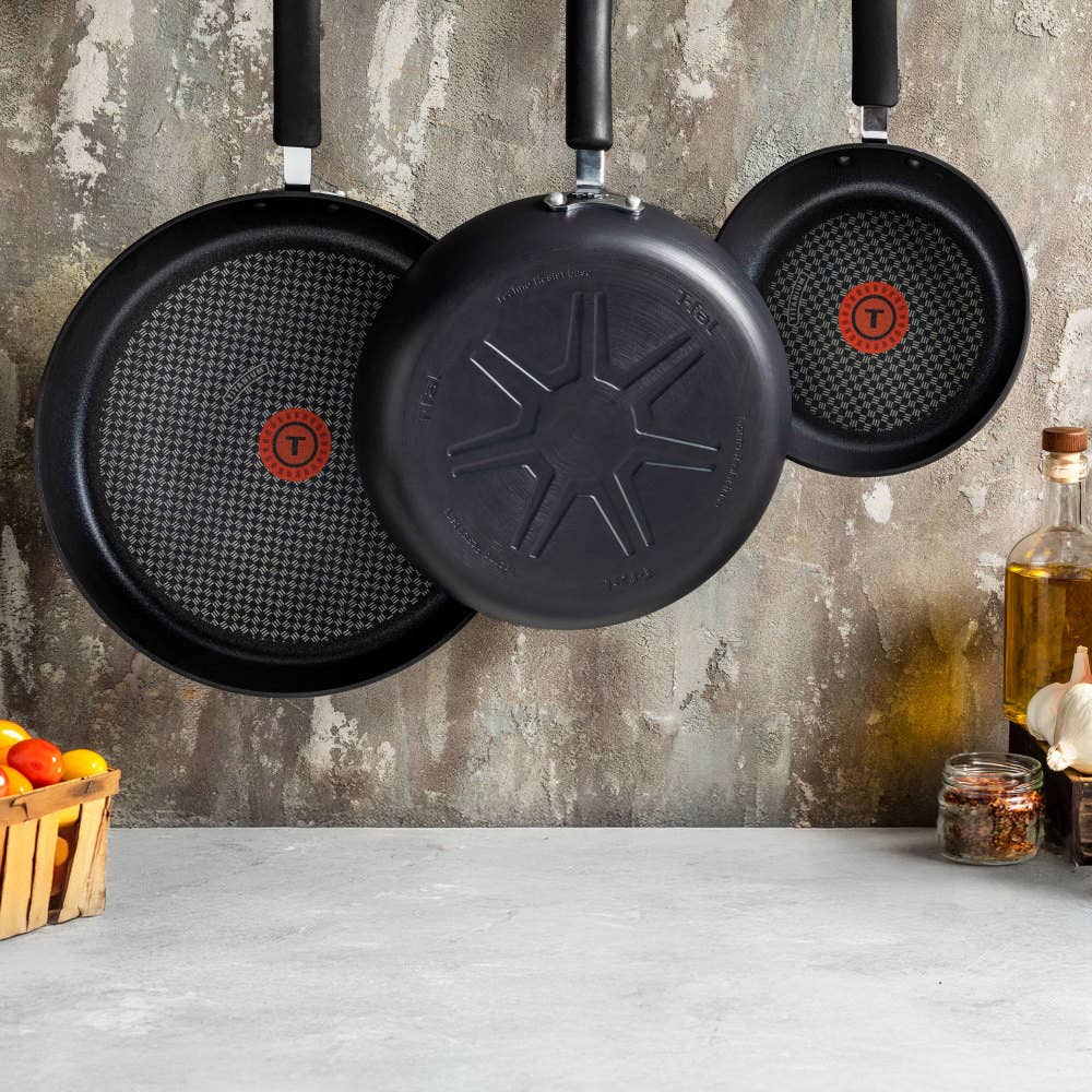 Three nonstick frying pans with red heat indicators hang on a kitchen wall.