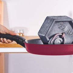 A pink frying pan holding a grey 22 lb weight, with a hand grasping the handle