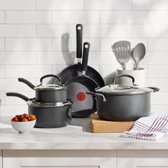 Nonstick cookware set with pots, pans, and lids on a kitchen counter, and white wall.