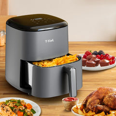 T-fal Easy Fry Max Air Fryer on a kitchen counter, surrounded by plates of colorful dishes, including chicken, vegetables, and desserts. The basket is open, showing crispy fries.