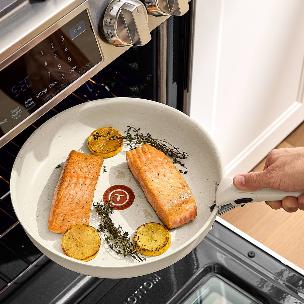Hand placing a beige pan with salmon and lemons into an oven. Salmon is golden brown