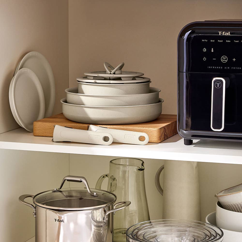 Stacked beige cookware on wood, stainless steel pot, glass bowls, plates, and an air fryer