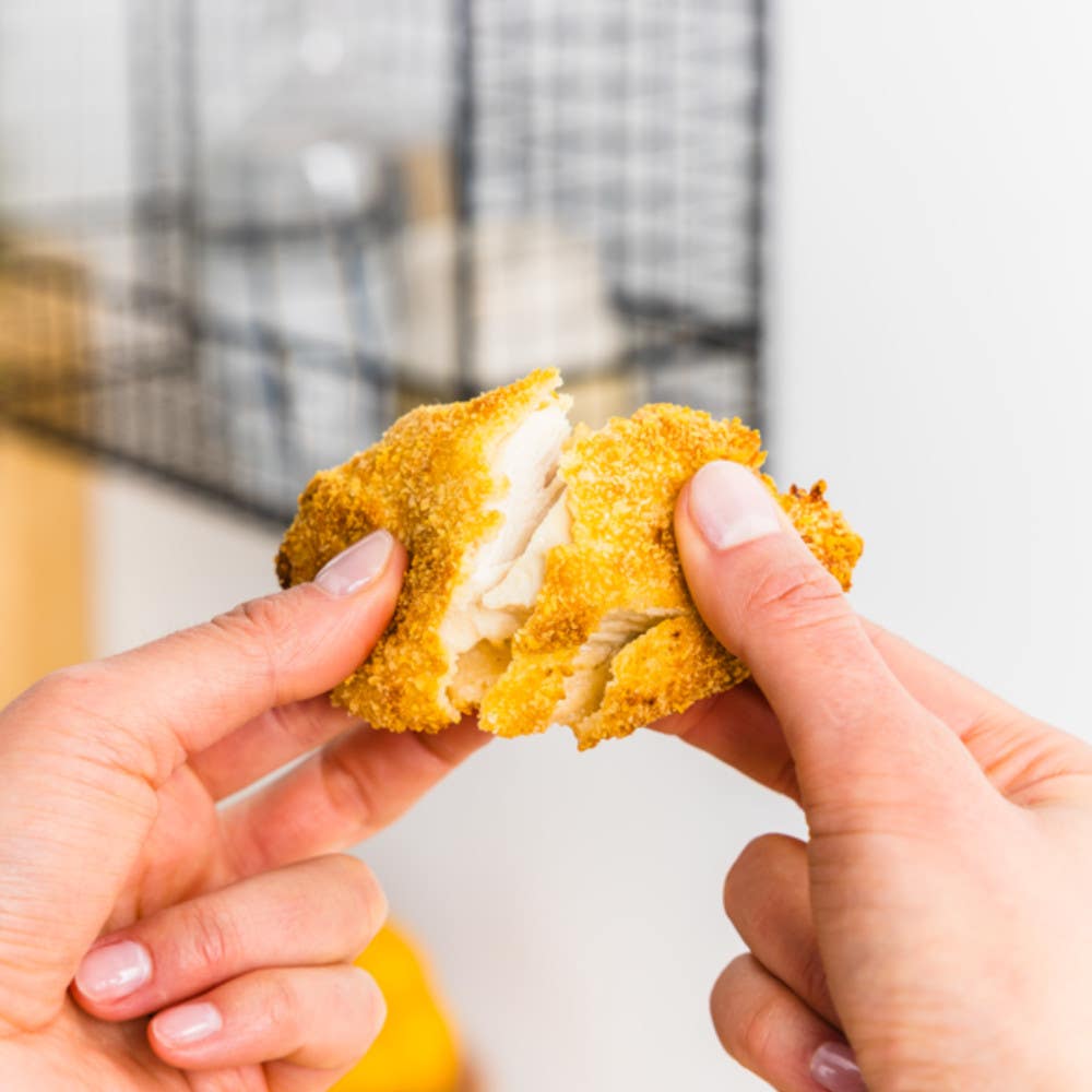 Hands spliting a chicken nuggfet in two.