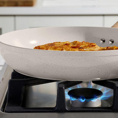 Close-up of a beige speckled ceramic frying pan on a gas stove with food cooking inside