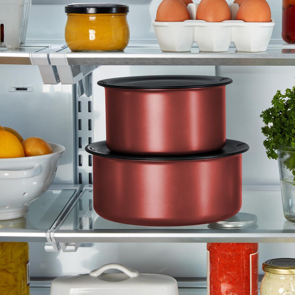 Stacked red pots with black lids in a refrigerator, surrounded by other food items
