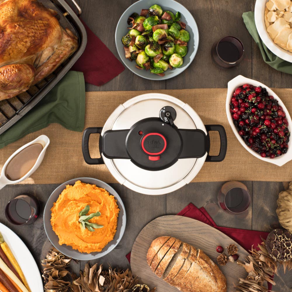 Various Thanksgiving dishes surround a pressure cooker on a table, including turkey, mashed potatoes, bread, and vegetables.