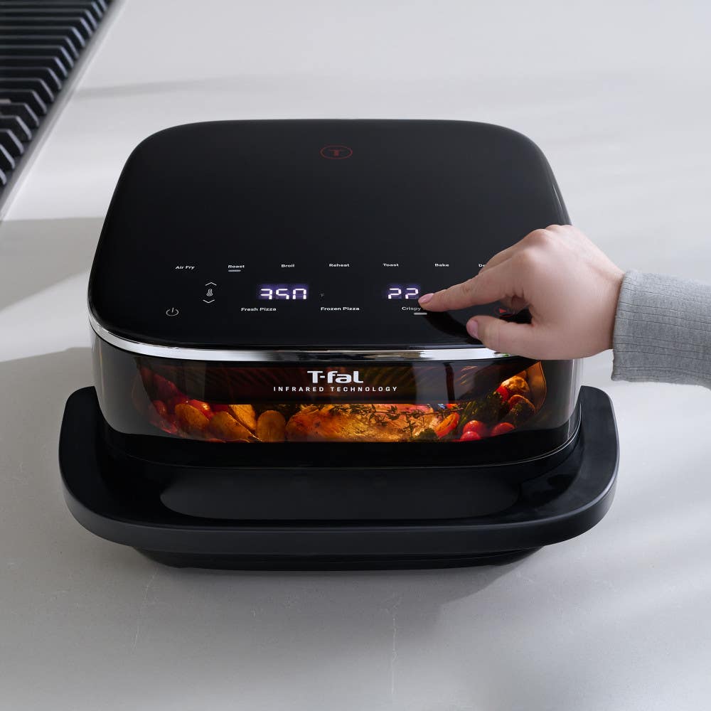 Infrared Surface XXL Air Fryer by T-fal, black unit with digital controls, a hand adjusting settings, food visible cooking through the front window
