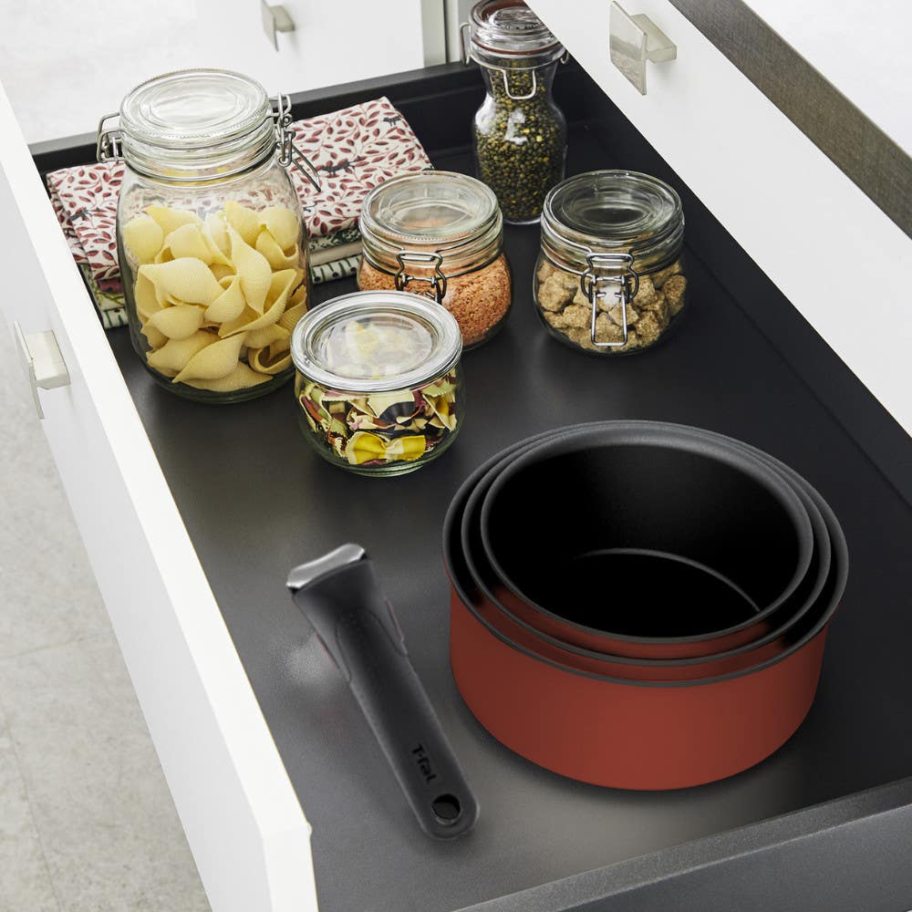 Stacked red pots with a detachable handle in a drawer next to jars filled with dry food