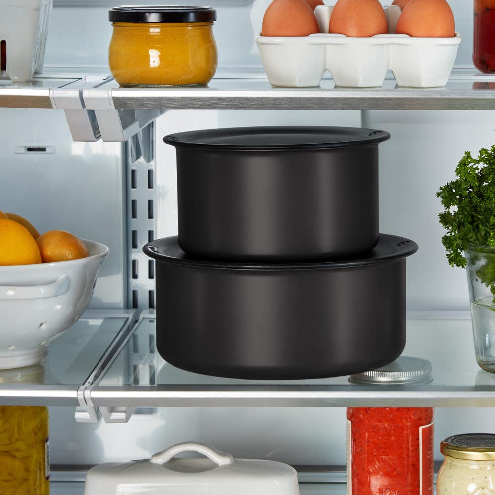 Stacked black pots with black lids in a refrigerator, surrounded by other food items