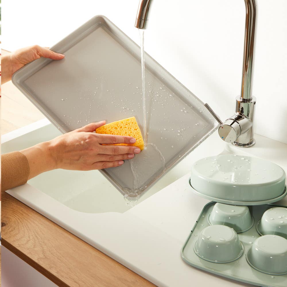 Person washing baking tray under running water in kitchen sink.