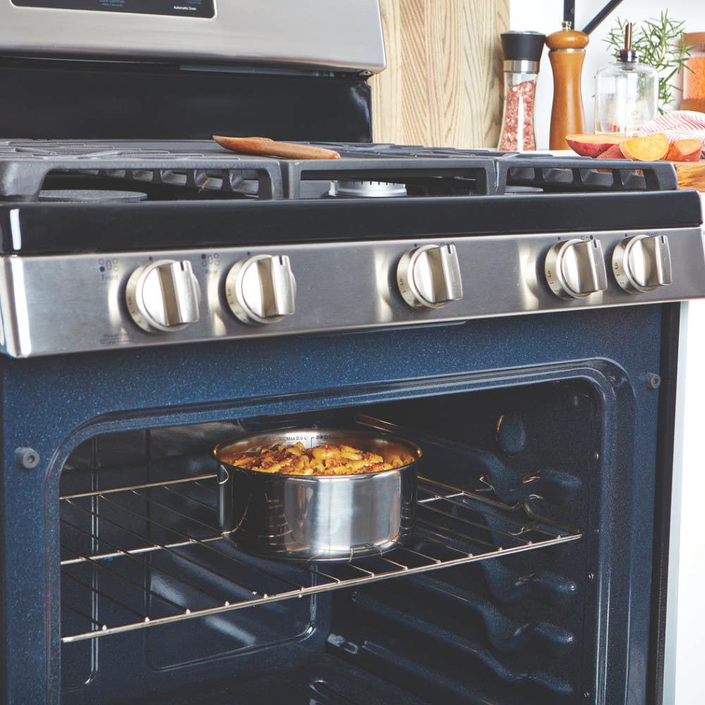 Stainless steel pot with food inside an oven, cooking. Various spices and utensils nearby