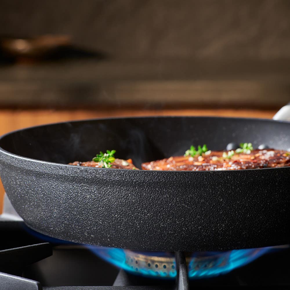 Stone Force Frying Pan on a gas stove with food and herbs.