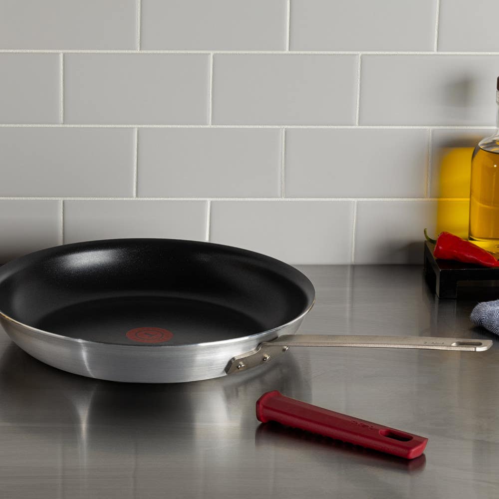 A nonstick frying pan with stainless steel handle and red silicone removable sleeve over