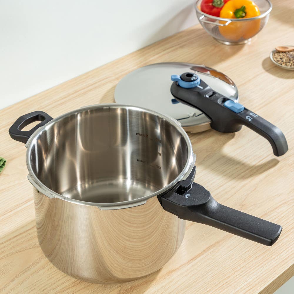 Open stainless pressure cooker with lid nearby on a wood counter with fresh vegetables